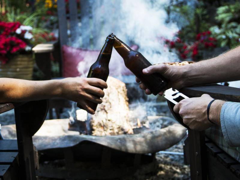 A couple clinking their beer bottles together while one holds the Barbarian Bar Tools' Simple Tool,