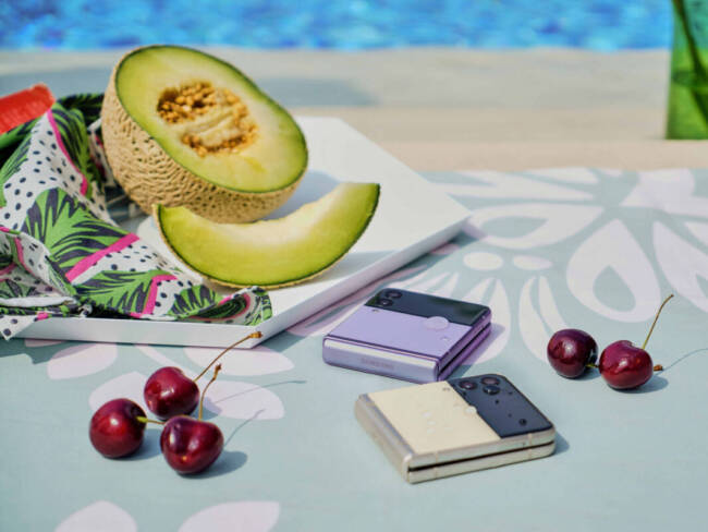 Cherries, a sliced honeydew melon, and two Samsung Galaxy Z Flip3 phones by a poolside; I wish I was there right now