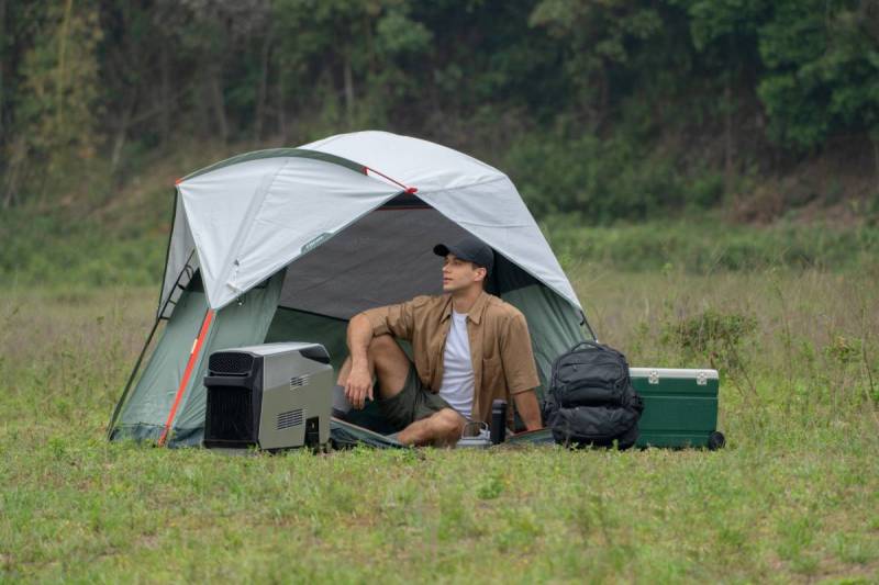 Man sits by tent enjoying cool breeze from the EcoFlow Wave portable aire conditioner.
