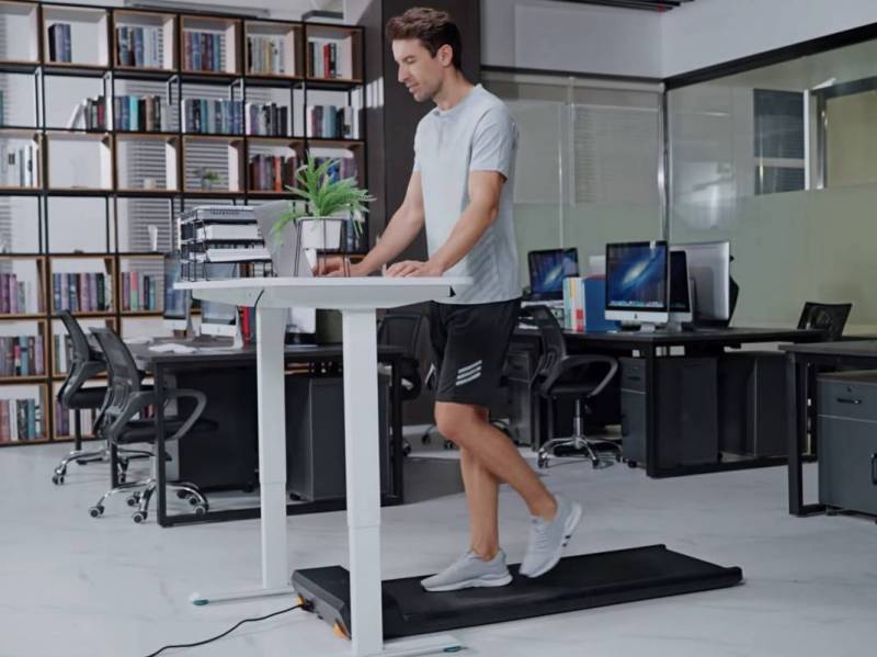 A man works at a standing desk while walking on a WalkingPad A1 Pro