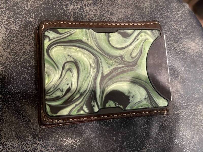 The Carved Alloy Wallet lying on top of the author's leather bi-fold wallet