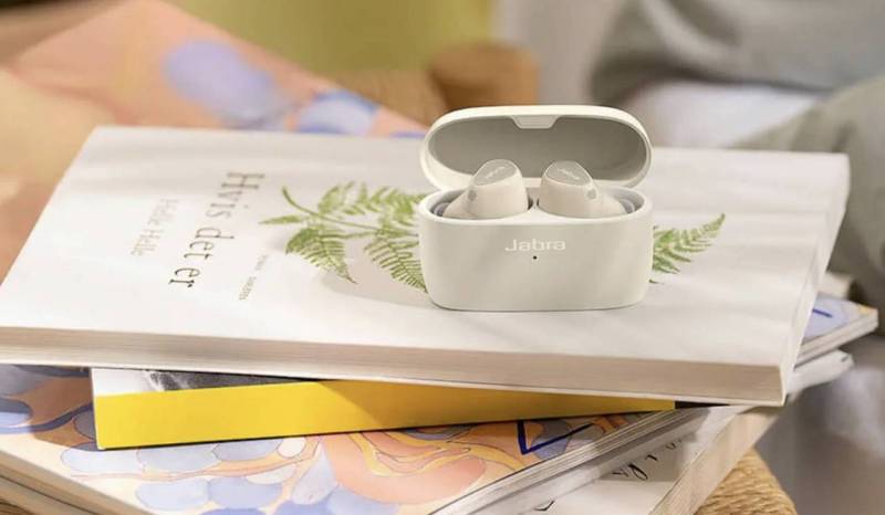A white Jabra Elite 5 case on a pile of books; the case is open and showing the earbuds.