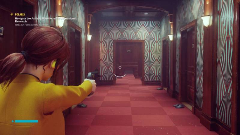 Jesse, wearing a yellow sweater, walks downa clong corridor with red-checkered carpet with her drawn gun. There are doors with lights on either side of the hallway, and most doors have a pair of shoes sitting just outside them.