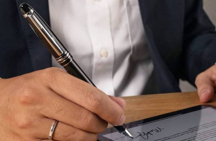 A person holding the Adonit Star Stylus while signing their signature in a document on an iPad. 