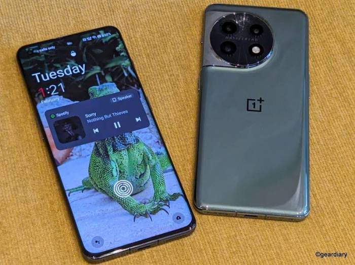 Two OnePlus 11 5G smartphones lying next to each other; on the left, the display is shown with a Spotify widget showing the Nothing But Thieves' song "Sorry." On the right, you can see the green back of the second 11 5G showing the new, round camera module. 
