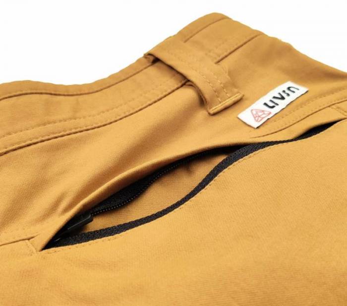 A portion of a pair of yellow LIVSN Ecotrek Trail Shorts is shown, including the waistband, a belt loop, and a zippered right hip pocket. 