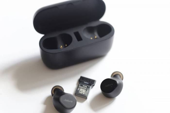 The Jabra Evolve2 True Wireless Earbuds charging case with the two earbuds lying on the table next to the included dongle