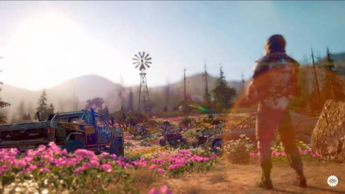 Scene from Far Cry New Dawn showing a male character looking at a field of flowers with a blue pickup truck on the left and a windmill in the distance with mountains in the background. 