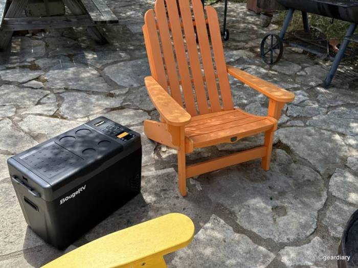 The BougeRV CRPRO30 30 Quart Portable Fridge sits between an orange and yellow Adirondack chairs.