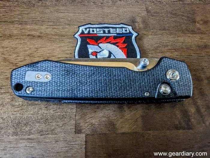 Photo shows a closed Vosteed Raccoon button lock knife lying on a Vosteed patch