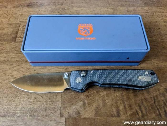An opened Vosteed Raccoon button lock knife next to its blue retail box