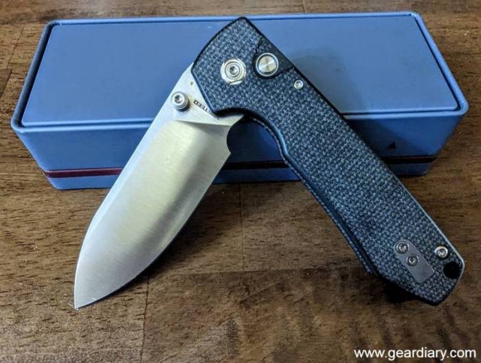 The Vosteed Raccoon button lock knife partially opened in front of its blue retail box