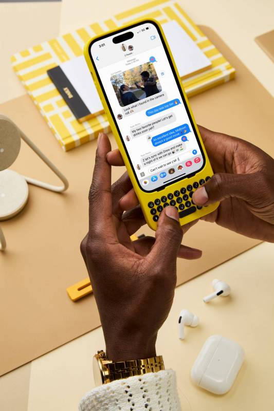 A person's hands hold an iPhone in a yellow Clicks creator keyboard while typing a text response