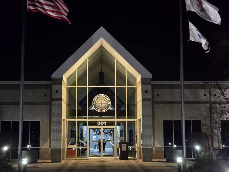 Flags wave outside a building at night.