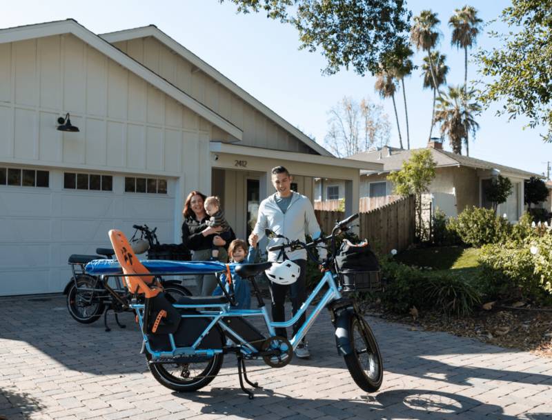 A family of three stands by the Rad Power Bike's RadWagon 5 Electric Cargo Bike.