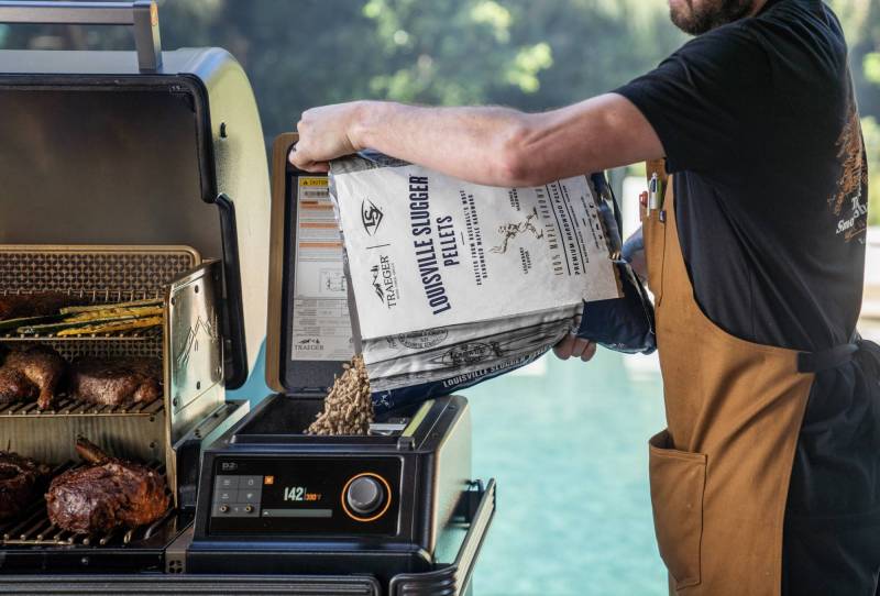 Person pouring the limited-edition Traeger Louisville Slugger Pellets into his barbecue smoker's hopper.