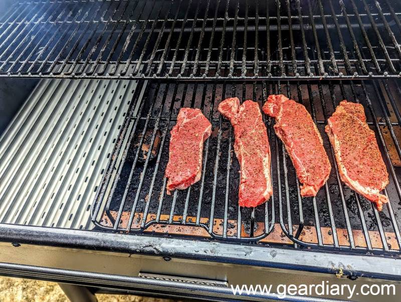 Steaks smoking on the regular grill grate in preparation for searing.