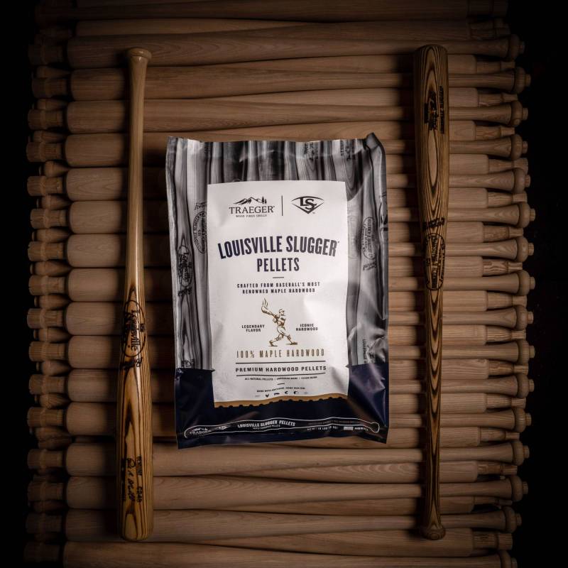 A bag of Limited-Edition Traeger Louisville Slugger Pellets resting on a pile of unfinished maple wood baseball bats.
