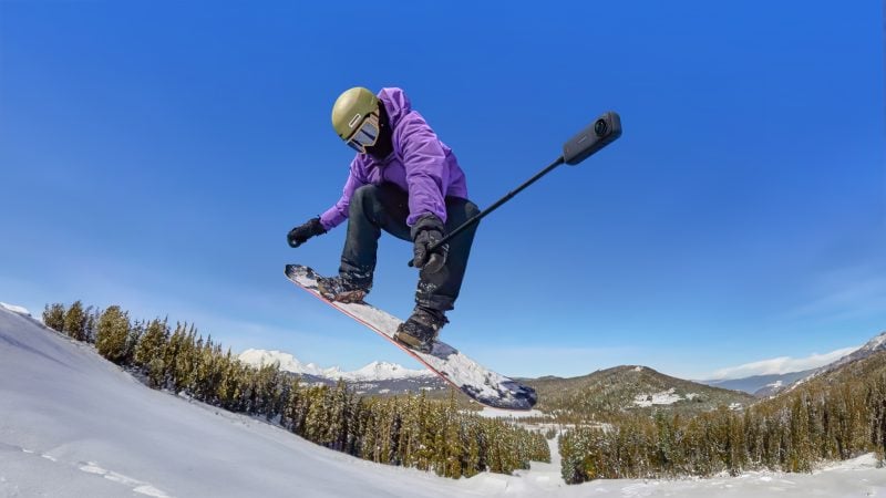 A snowboarder holding the Insta360 X4 on a selfie stick while making a jump
