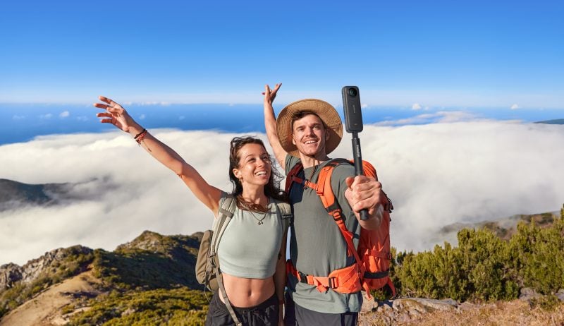 A man and a woman taking a photo on the edge of a mountain while using the Insta360 X4 on a selfie stick.