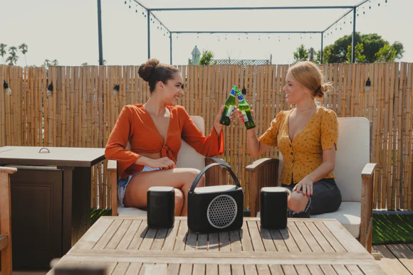 Rocksteady Stadium 2-Speaker and Subwoofer Pack sits on a table in front of two seated women clinking their drinks together.