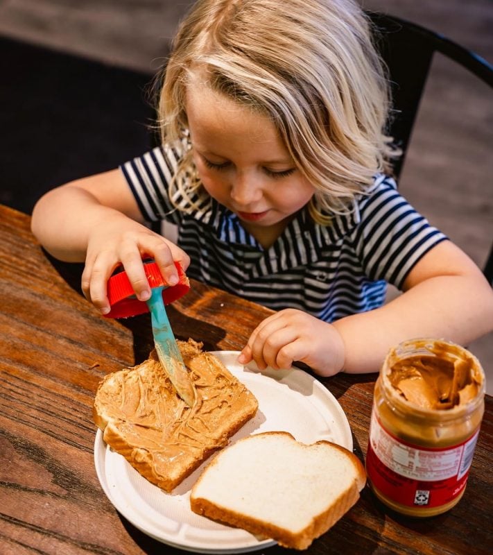 Child using Simple Spread to put peanut butter on their sandwich.