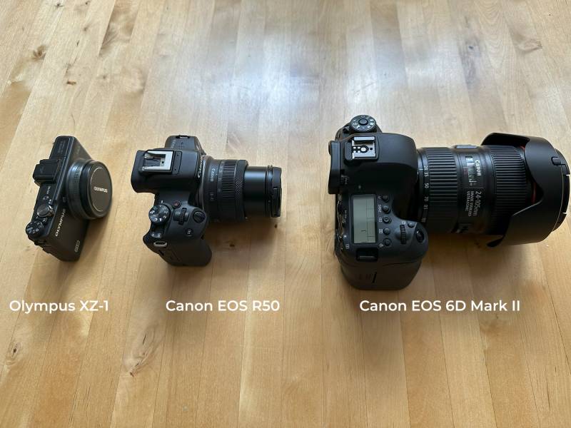 Size comparison of an Olympus XZ-1, the Canon EOS R50, and the Canon EOS 6D Mark II