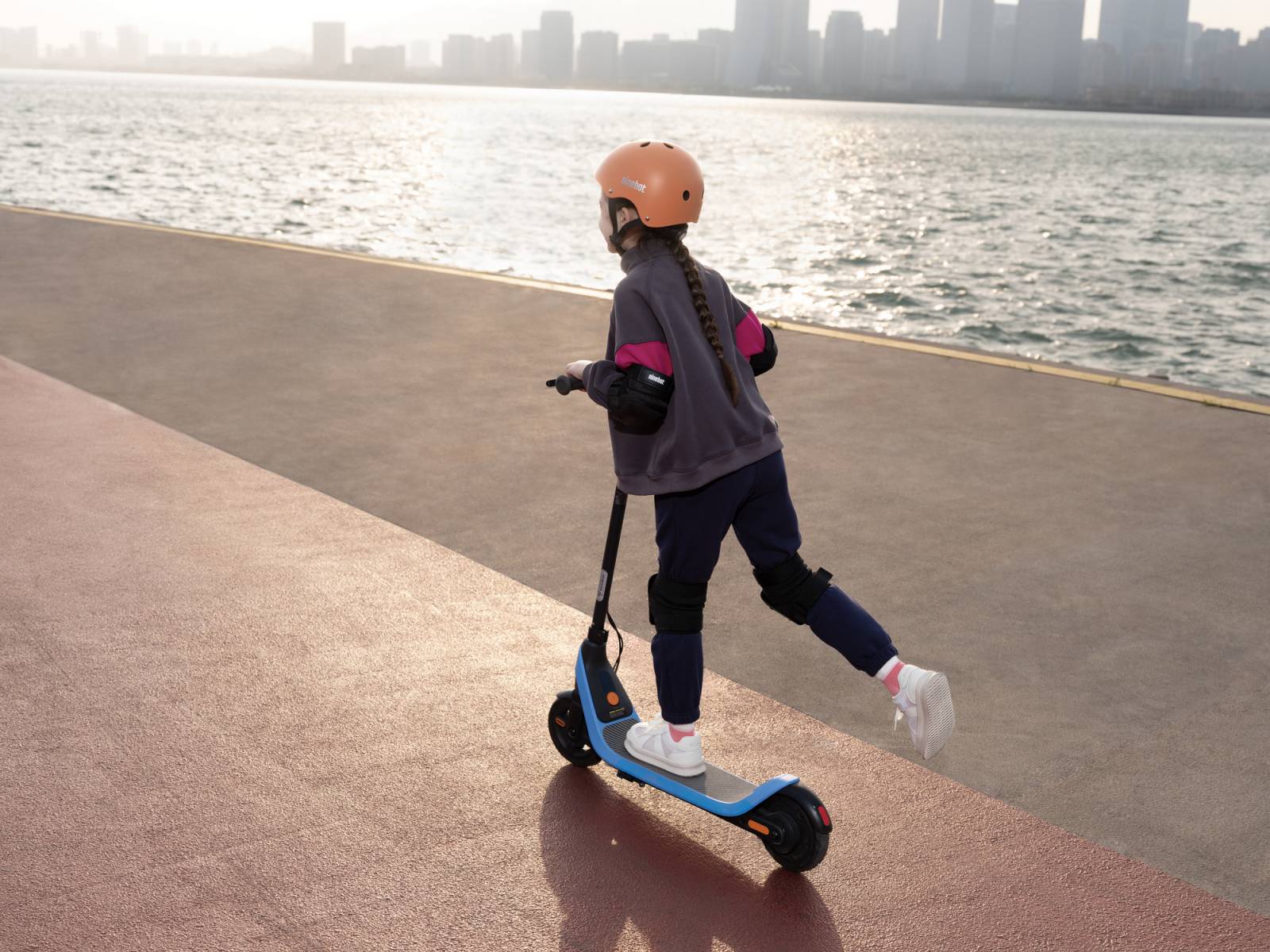 A girl riding the Ninebot eKickScooter C2 Lite down a path near water.