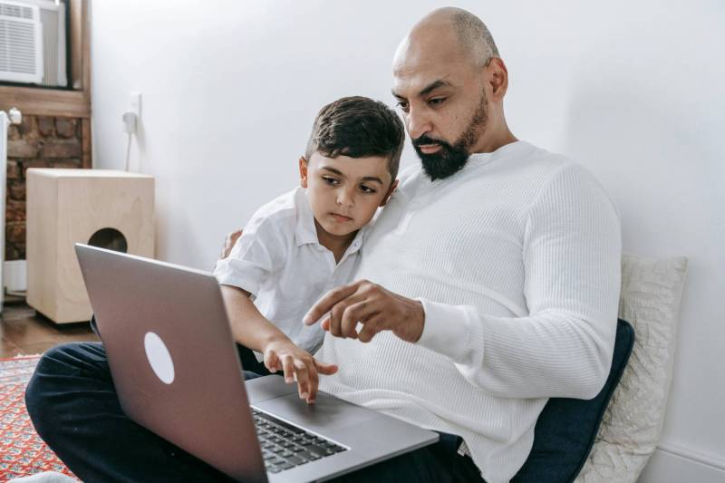 Father and son sitting on the floor together and looking at a computer