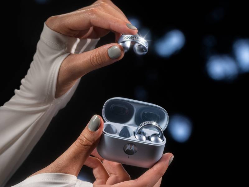 The Brilliant Collection - a white-sleeved hand with gray nail polish holding the moto buds loop case while the other hand holds one of the ear buds