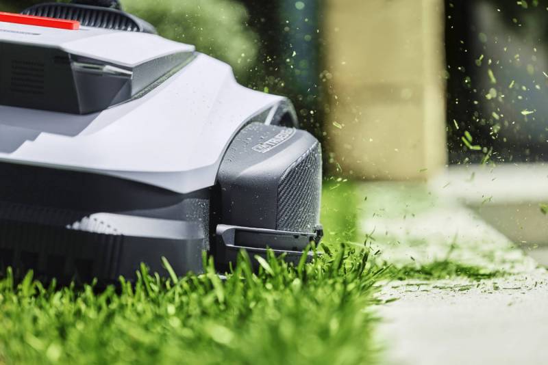 ECOVACS GOAT Charges into Lawn Care with LiDAR Mapping and a Built-In TruEdge Trimmer 3 The ECOVACS GOAT robot mower trimming the edge where a lush green lawn meets a concrete walkway.
